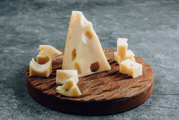 Piece of cow's milk Maasdam cheese on wooden cutting board over concrete background.