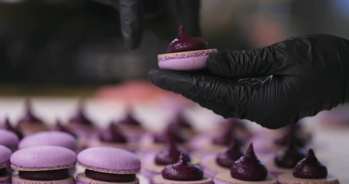 Process of making macaron macaroon, french dessert. Assembly of two halves with stuffing. Hands in black gloves