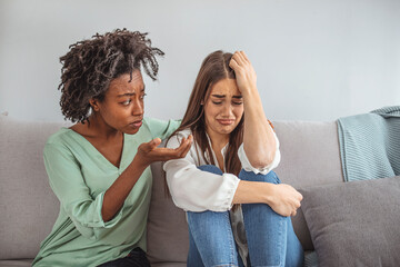 Friend trying to calm down her friend. Woman crying. Young lady sharing her problem with friend. female in depression. Woman omforting hes sad friend sitting on a couch in the living room at home