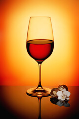 the glass of red wine on orange gradient background with a flower near the glass. 