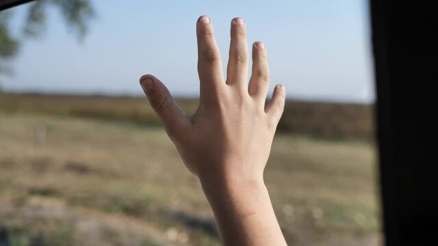 A teenager boy traveling by car waving at the open window of the car. slow motion. breathing the fresh air of the countryside, his hand moving in the wind.