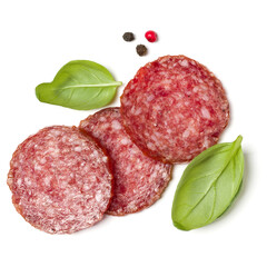 Slices of salami isolated on white background closeup. Sausage and basil leaves top view.