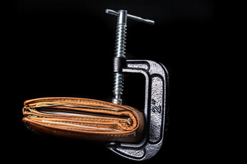 Leather wallet with money squeezed by a metal clamp. Taxpayers' money devoured by taxes and inflation.