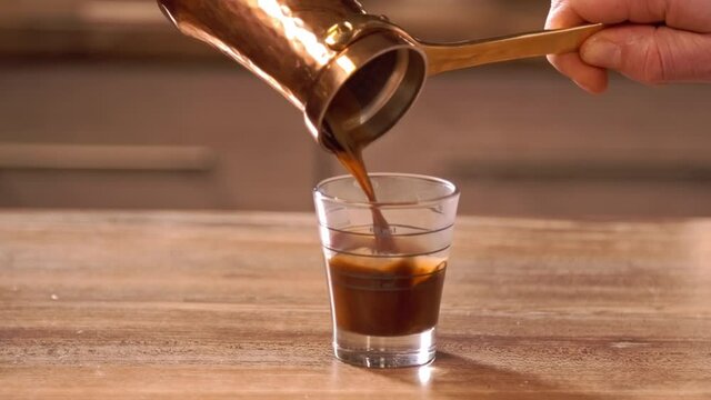 Pouring fresh coffee from copper Ibrik into transparent glass 