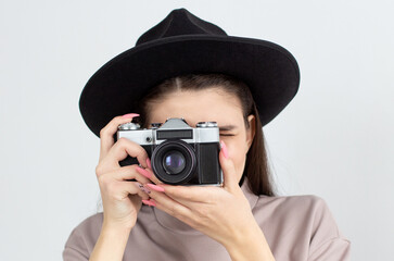 European woman holding retro photocamera and taking a photo over white background in studio