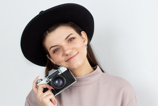 European woman holding retro photocamera and smiling over white background in studio
