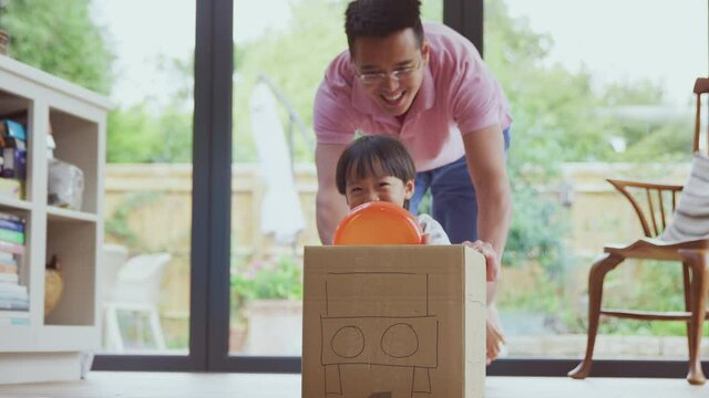 Asian father and son having fun pushing boy around kitchen floor at home in junk modelled car - shot in slow motion 