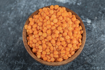 A wooden bowl full of raw lentils on a gray background