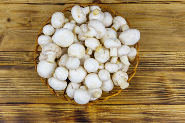Fototapeta na wymiar Fresh champignon mushrooms in wicker basket on the wooden table. Top view
