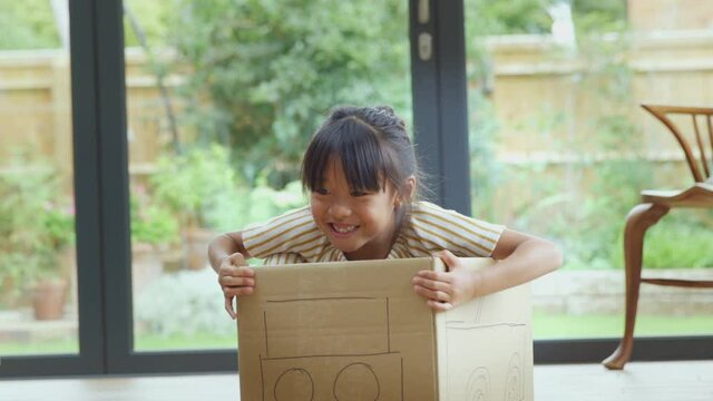 Asian girl having fun playing in junk modelled car on kitchen floor at home - shot in slow motion 