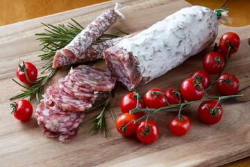 Sliced Air-dried salami with rosemary and cherry tomatoes - wood background