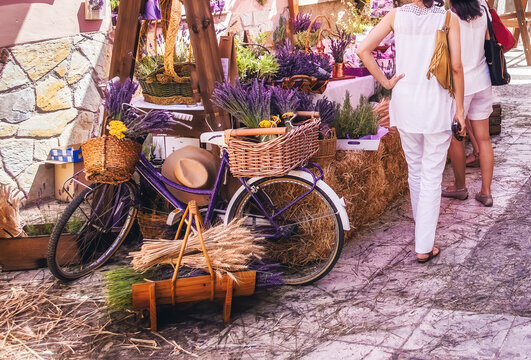Fototapeta two women dressed in white walking through a street market in front of a stall with lavender products at the lavender festival in Brihuega, Guadalajara Spain