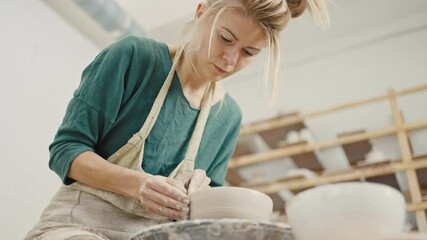 Concentrated woman working on pottery wheel, making ceramic bowl, below view, slow motion