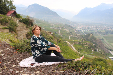 Naklejka premium Woman sitting on the white cloth on the ground where there are some fresh ripe grapes, background has spectacular view of Mountains.Wine production region. Green landscape.
