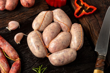 Beef and pork sausages, sausage and raw sausages on wooden board with vegetables, pepper, garlic, rosemary, bell pepper and knife.