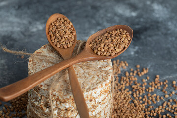 Two wooden spoons of raw buckwheat and crispbread on marble surface
