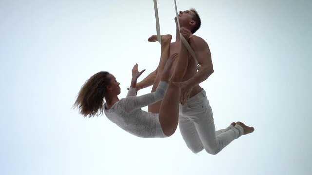 Aerial straps duo wearing white costume on white background doing performance 
