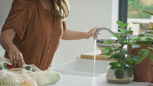Close up of Asian couple washing fresh and healthy fruit and vegetables in zero waste packaging from bag in kitchen at home - shot in slow motion