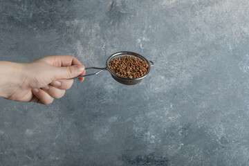 Female hand filtering raw buckwheat with strainer