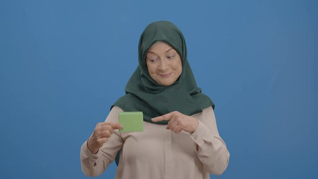 Elderly woman in a turban holding a green box in her hand is isolated on a white background. The old lady pointing at the green box draws attention. Creative people can put whatever product they want.