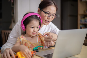 .A mother is wearing headphones for her daughter to help her study online.