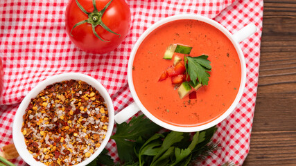 Traditional gazpacho on a wooden table with different seasonings and herbs. Top view.