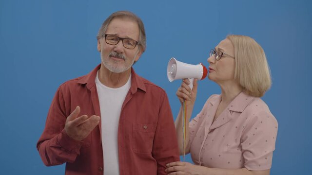The old woman shouts with a megaphone to her husband, who never listened to him and did not value his thoughts. The husband still does not listen to his wife.Blue background.