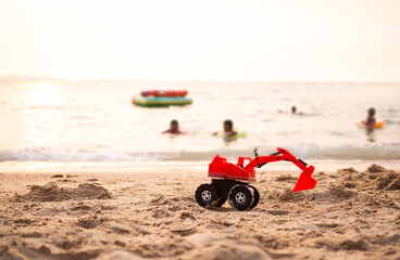 Toy tractor on sand beach at coast with child playing on sea blured. sun set on ocean. tourist in travel summer holidays. pappy family concept.