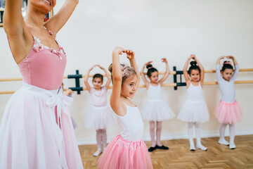 Female teacher exercising with a group of little girls dancing ballet in the class.