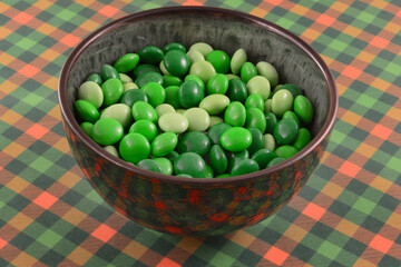Saint Patrick's Day green candy coated dark chocolate mint candy in bowl on green and orange check...