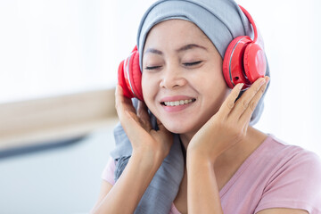 Happy a asian women disease mammary cancer patient with pink ribbon wearing headscarf in headphones...