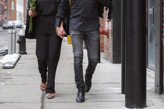 Stylish adult couple wearing black walking down the street holding each other's hand. Legs shot. Fashion blogging relationship concept