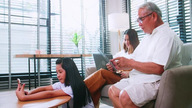Grandpa, mother and daughter use wireless technology while relaxing in the living room. Asian family is enjoying the modern mobile technology in their home.