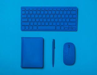 Blue pen, notebook, keyboard and mouse on a blue background. Flat lay.