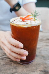 The woman held a glass of strawberry syrup, soda shot, espresso and fresh strawberries in a glass, drank it and put it on a wooden table. 