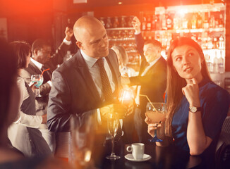 Smiling man enjoying conversation with young female colleague on corporate party in bar