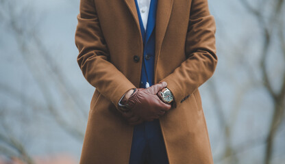 Selective focus of an elegant man wearing a classic brown coat with leather  gloves