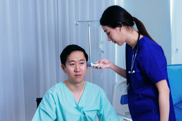 Young female medical worker with stethoscope examining ears of Asian male patient in uniform using...