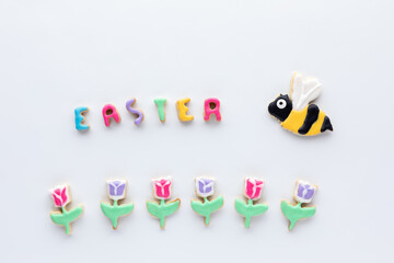 Sugar cookies in the shapes of tulips with a bee and the word Easter against a white background.