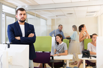confident businessman with arms crossed in busy modern coworking space