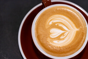 Cappuccino with foam in the form of heart on a black table background top view