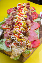 Comida rápida venezolana hecho de carne, pollo, lechuga, ensalada de col, tomate, papas al hilo, queso rallado, tomate, tocino con pan baguette, en mesa de madera para restaurante