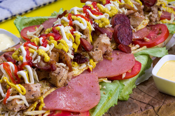Comida rápida venezolana hecho de carne, pollo, lechuga, ensalada de col, tomate, papas al hilo, queso rallado, tomate, tocino con pan baguette, en mesa de madera para restaurante