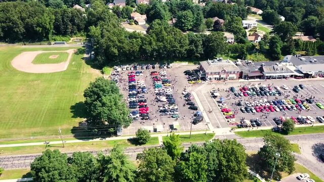 Aerial view away from parking lots full of old, vintage and sport cars, sunny day - reverse, tilt up, drone shot