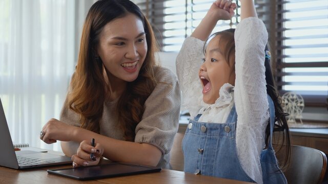 Asian Young Mother Working With Laptop Computer At Home And Help Daughter Doing Homework, Single Mom Freelancer Work From Home And Helping His Girl Kid Teaching Homework On Desk