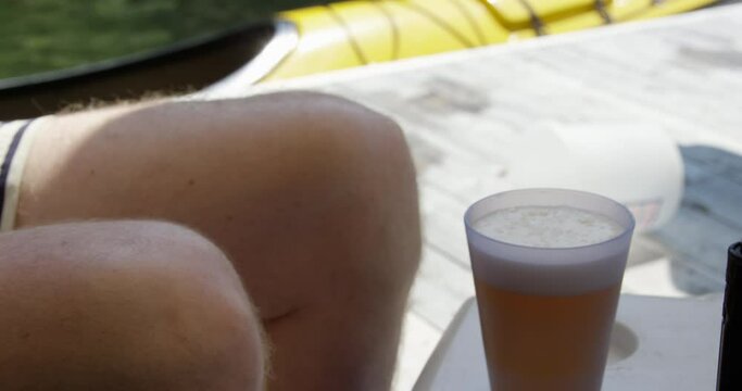 Man sitting by kayak on dock drinking a beer - close up on legs and beer