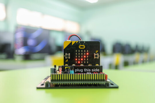 Microbit Educational microcontroller board showing a checkmark. With a backdrop of a computer room in the concept