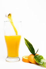Pouring orange juice into glass with pieces of oranges and greenorange  leafs on black background. Abstract.