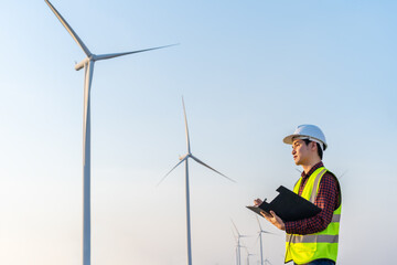 male engineer working and writing on clipboard against wind turbine farm