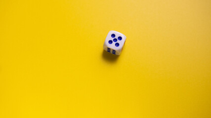 White dice with round dots number five on yellow background close-up. Concept of gambling and chance